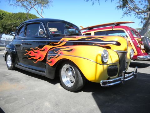 1997 Ford Ranger - A classic hot rod with vibrant flame graphics is parked next to a wood-paneled station wagon carrying surfboards.