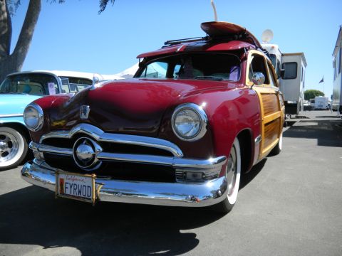 1997 Ford Ranger - A classic red woody wagon with a surfboard on its roof is parked outdoors next to another vehicle.