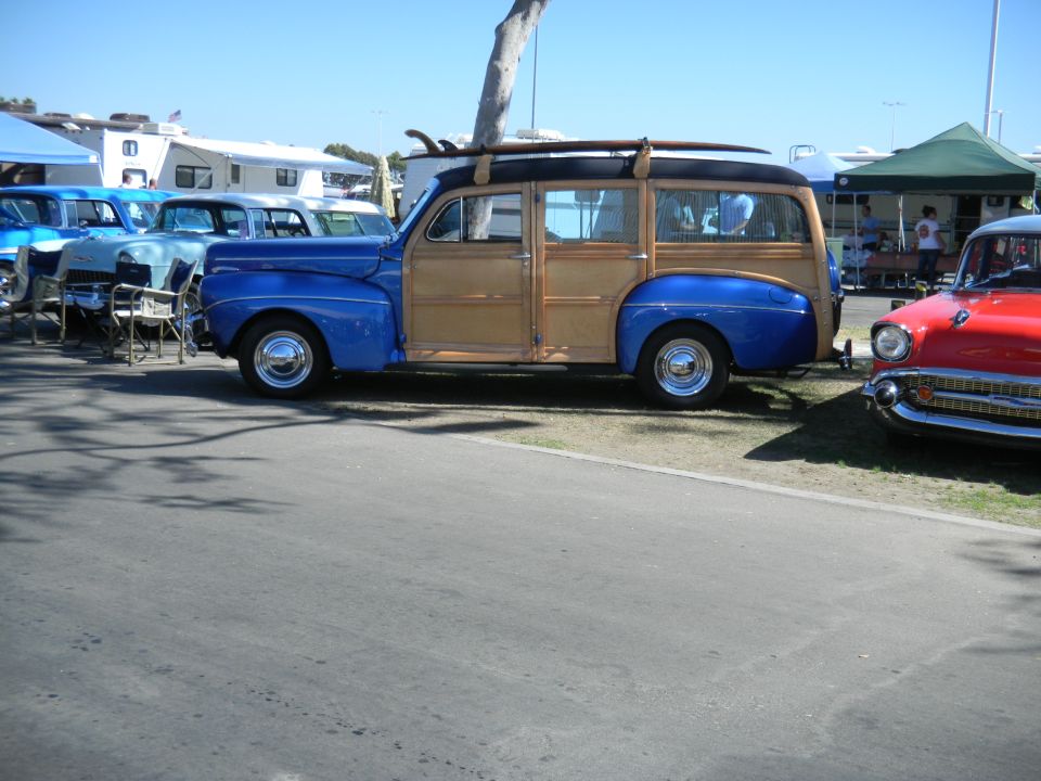 Blue and wood-paneled station wagon with surfboards on roof parked next to a red car