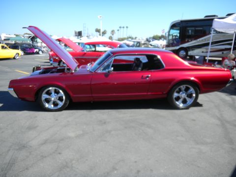 1997 Ford Ranger - A shiny red classic coupe is displayed with its hood up at a car show, alongside other vehicles.