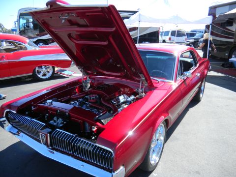 1997 Ford Ranger - A red 1967 Mercury Cougar is displayed with its hood open at a car show, alongside other vehicles.