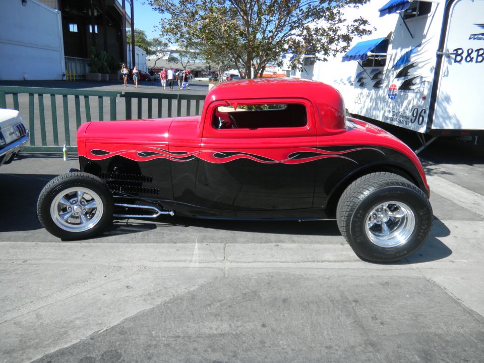 Red and black hot rod coupe with flame decals on the side. It has large rear tires and chrome wheels