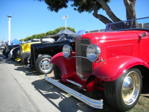 1997 Ford Ranger - A line of classic cars, including a bright red hot rod, are parked outdoors on a sunny day.