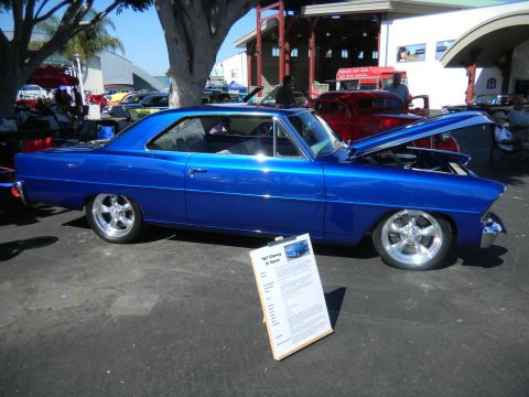 1997 Ford Ranger - A bright blue 1967 Chevrolet Nova SS coupe is displayed with its hood open at a car show, accompanied by an information board.