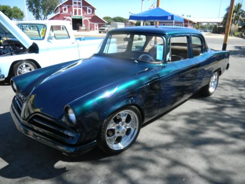 1997 Ford Ranger - A classic sedan with a metallic paint job is displayed at an outdoor event with a pickup truck nearby.
