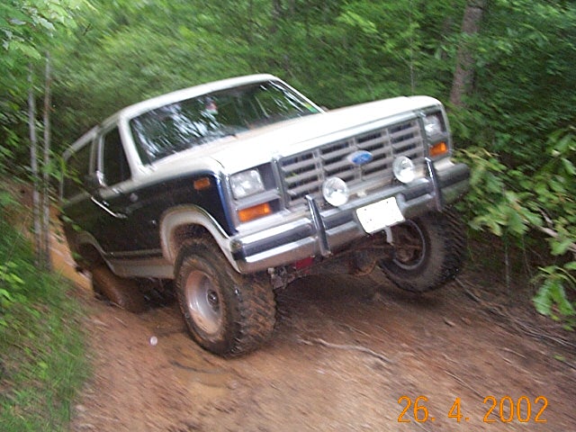Black two-tone Ford Bronco with grille guard on a muddy forest trail