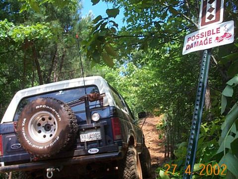 1986 Ford Bronco - 1986 Ford Bronco navigates a wooded trail, with a warning sign indicating potential damage.