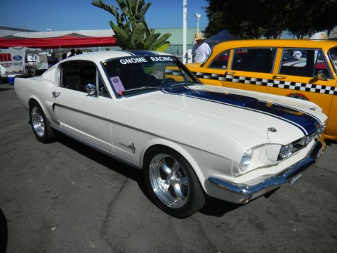1997 Ford Ranger - A classic white Ford Mustang with racing stripes is parked next to a yellow checkerboard taxi.