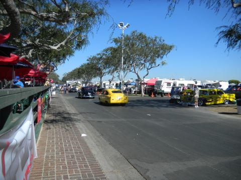 1997 Ford Ranger - A yellow car drives down a road lined with trees and spectators at an outdoor event.