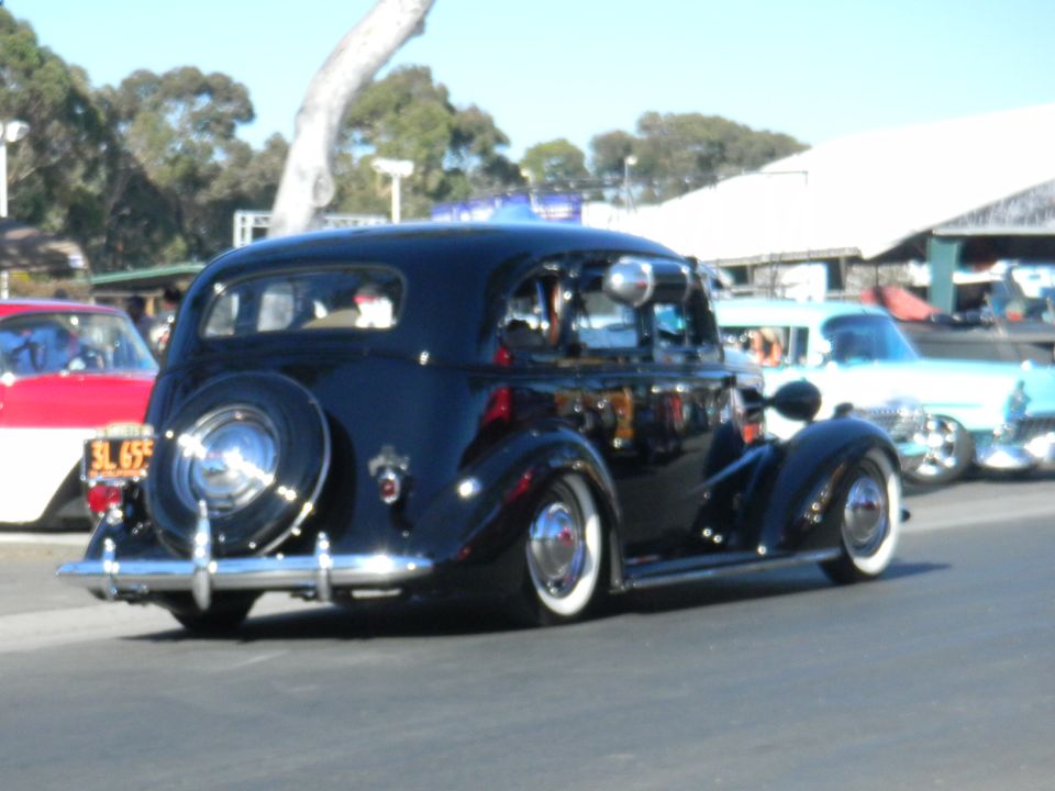 Black sedan with whitewall tires and a spare tire on the rear, seen from the back at a car show