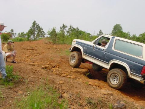 1986 Ford Bronco - Ford Bronco navigates a challenging off-road trail with spectators observing the action.