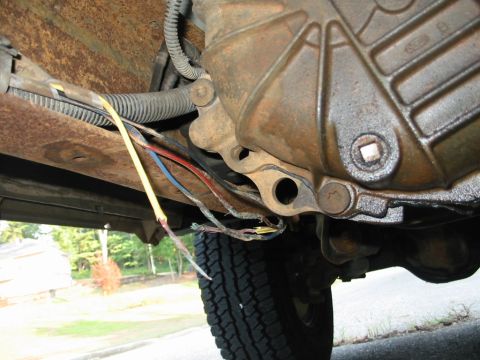 1988 Ford Bronco - Underside view of a vehicle's transmission area, showing a damaged trailer wiring harness with exposed wires.