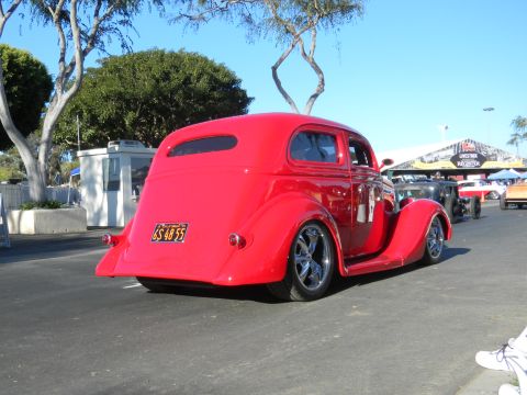 1997 Ford Ranger - A bright red hot rod coupe is parked at an outdoor event with other vehicles and tents visible.