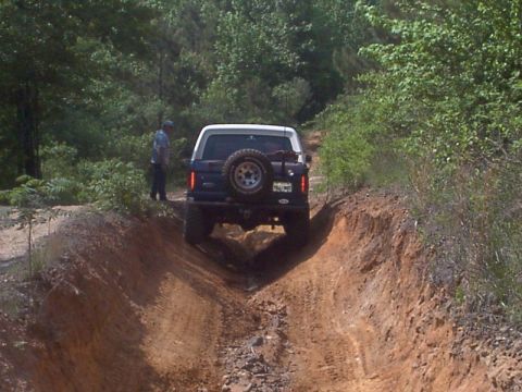 1986 Ford Bronco - A Ford Bronco navigates a challenging dirt path surrounded by dense foliage.