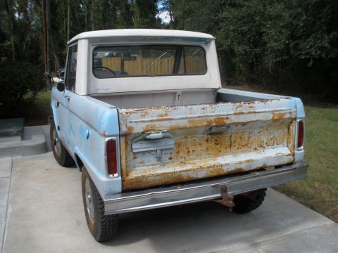 1966 Ford Bronco - Rear view of a 1966 Ford Bronco, light blue with a white hardtop, exhibiting rust on the tailgate.