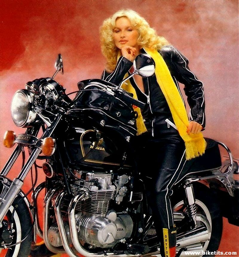 Black Honda motorcycle with a woman in leather sitting on it. Yellow scarf