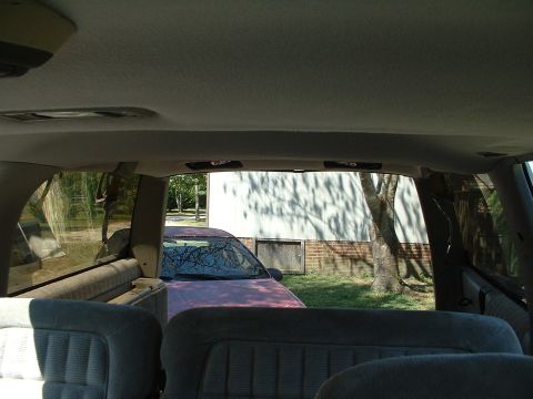 1994 GMC Suburban - View from inside a vehicle shows a purple car parked outside a building with trees casting shadows.