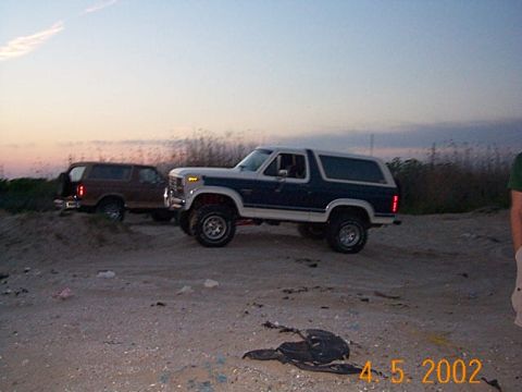 1986 Ford Bronco - Two Ford Broncos are parked on a dirt lot during dusk.