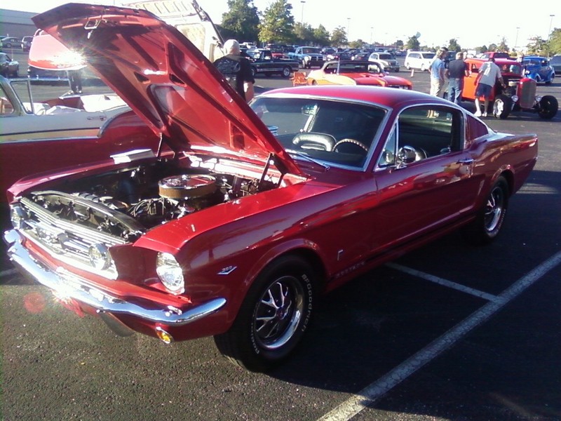 Red 1965 Ford Mustang Fastback with hood open, showing engine. Chrome bumpers and trim. BFGoodrich tires