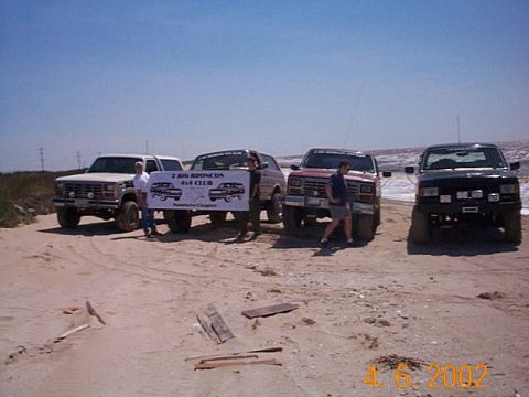 1986 Ford Bronco - A group of Ford Broncos gathered on a beach, with a banner indicating they are part of a 4x4 club.