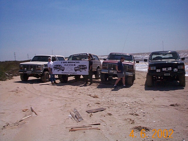 Four lifted Ford Broncos on a beach with a Texas Big Broncos 4x4 Club banner, 2002