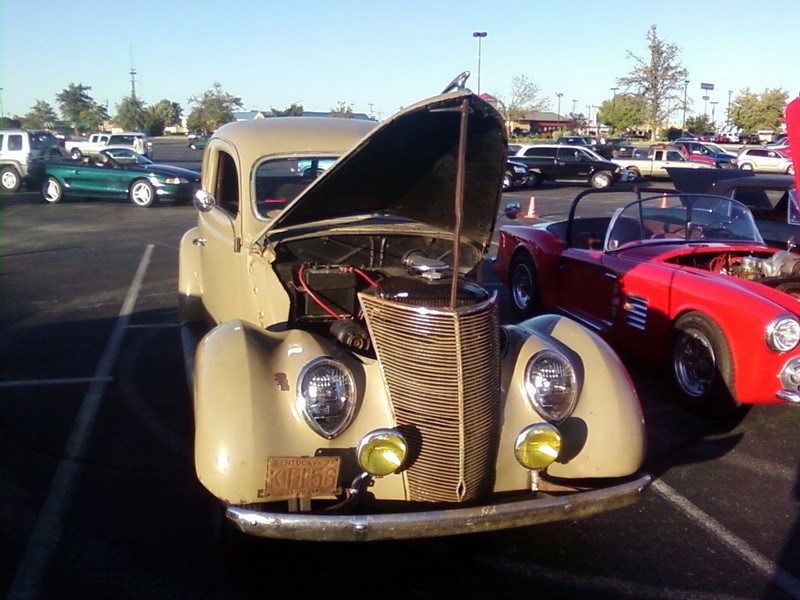 Tan 1939 Ford coupe with hood open, yellow fog lights, and license plate KHP56