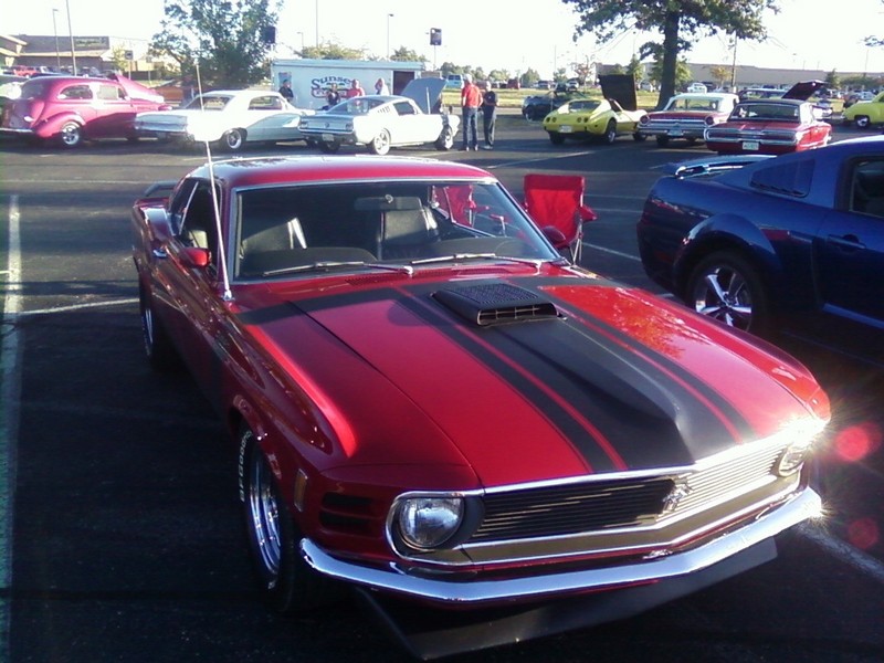 Red 1970 Mustang fastback with black hood stripes and hood scoop at a car show