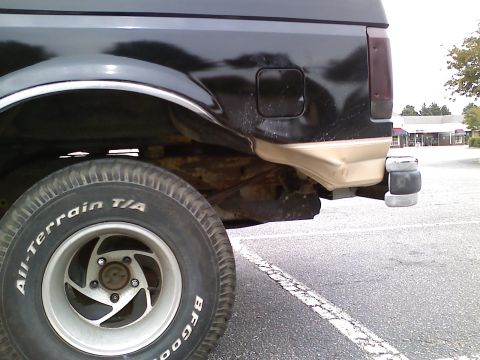 1990 Ford Bronco - Close-up of the rear quarter panel and tire of a black 1990 Ford Bronco, showing its tan lower trim and rear bumper.