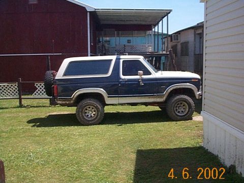 1986 Ford Bronco - A blue and white Ford Bronco is parked on a grassy lawn next to a white building.