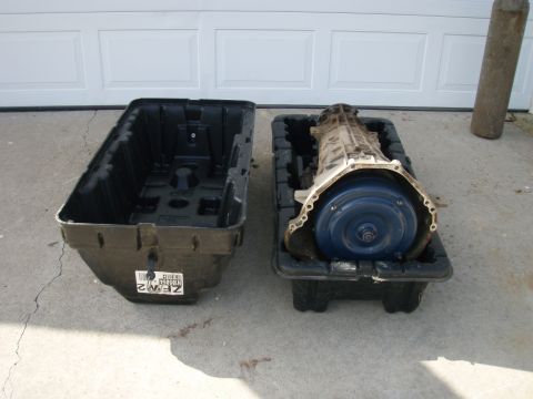 1994 Ford Bronco - A vehicle transmission and an empty storage container are placed on the ground in front of a closed garage door.