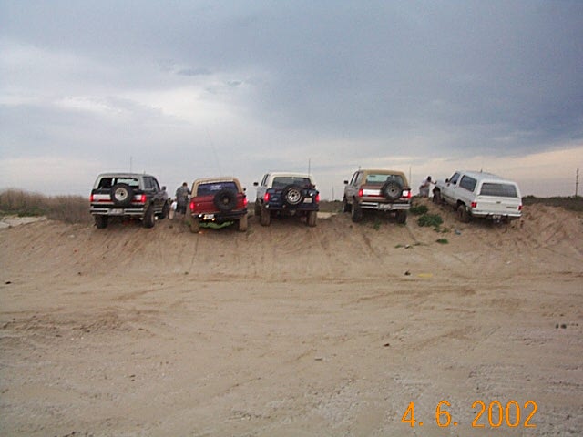 Five lifted SUVs parked in a row on a sand berm, rear view, 2002 date stamp