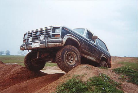 1986 Ford Bronco - This Ford Bronco is shown navigating a challenging off-road terrain with a clear blue sky overhead.