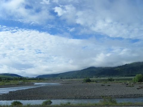 1981 Ford E350 - A vast, rocky riverbed flows towards misty mountains under a dramatic sky.
