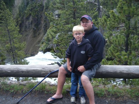 1981 Ford E350 - A father and son pose for a photo while sitting on a log, with a scenic river and forested canyon in the background.