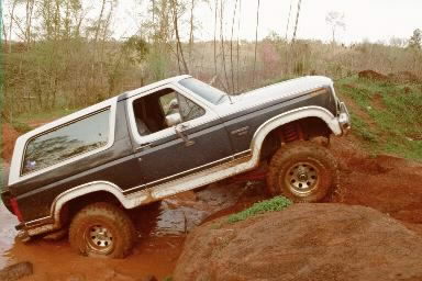 1986 Ford Bronco - This Ford Bronco is navigating a challenging off-road course with mud and rocks.