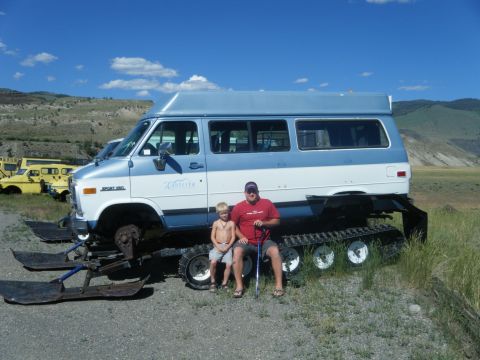 1981 Ford E350 - A modified van sits on snow tracks and skis, with two people posing beside it in a grassy, hilly area.