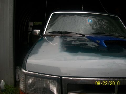 1993 Ford Bronco - The front end of a two-tone Ford truck is parked inside a garage, with rain visible on the windshield.