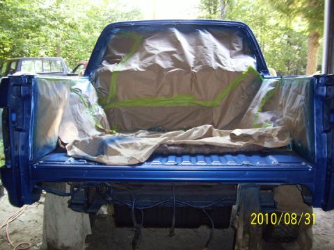 1993 Ford Bronco - A blue pickup truck bed is prepared for painting, with masking paper and tape covering the interior surfaces.