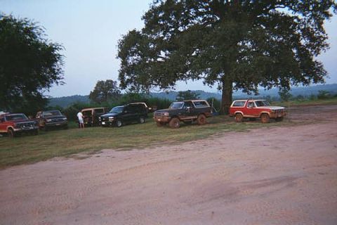 1986 Ford Bronco - Multiple Ford Broncos and other SUVs are parked together in a scenic outdoor setting.