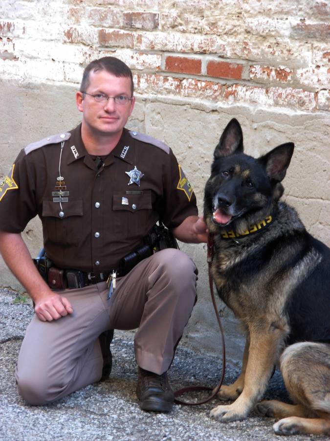 Sheriff's deputy kneeling beside a German Shepherd K9 wearing a yellow Sheriff collar