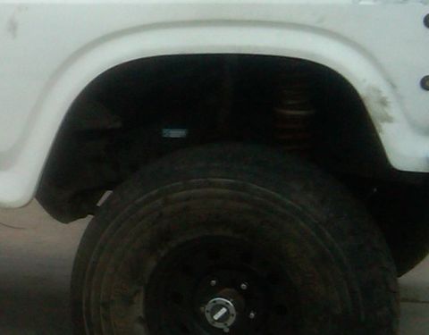 1986 Ford Bronco - Close-up of a white vehicle's rear wheel well and tire, with visible suspension components.