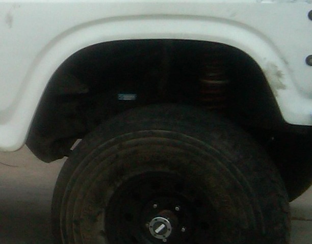 White vehicle's rear wheel well and tire, showing suspension and part of the body panel