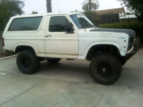 1986 Ford Bronco - This white SUV features a black hood and is lifted with large off-road tires.