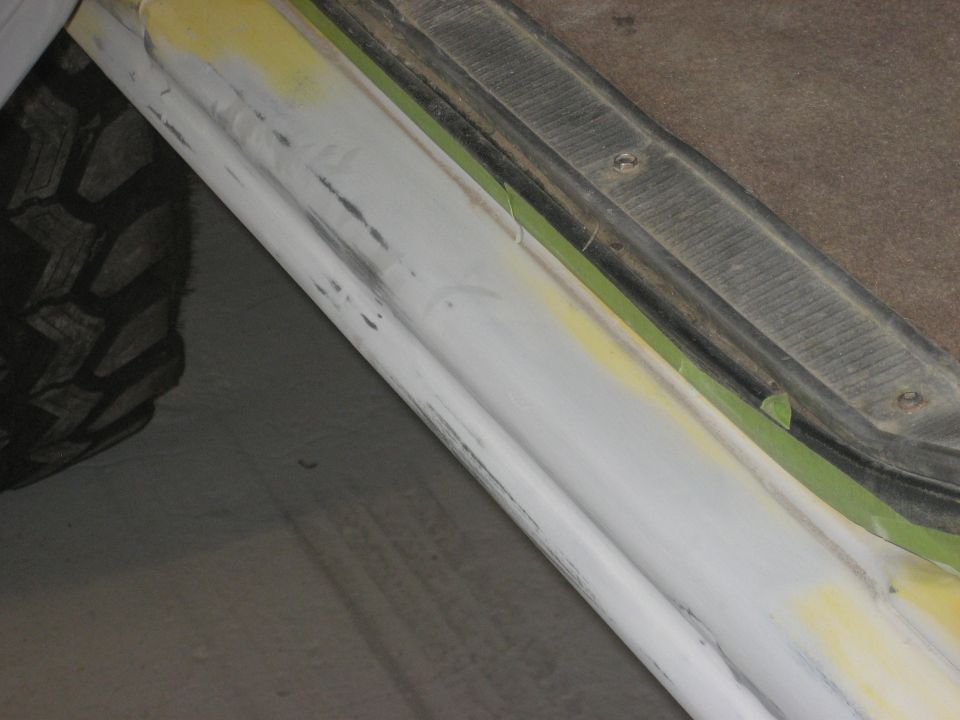 Close-up of vehicle door sill with body filler and masking tape, tire visible on left