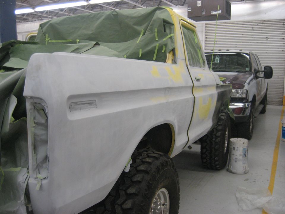 Ford Bronco body covered in primer and green tarp, parked next to a pickup truck
