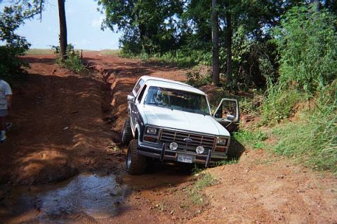 1986 Ford Bronco - 1986 Ford Bronco navigates a muddy, rutted dirt path with its driver's door ajar.