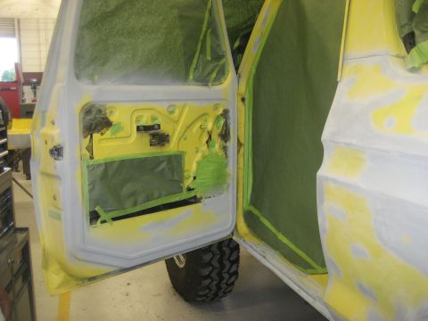 1978 Ford Bronco - The interior of a vehicle door is prepped for paint, with masking tape covering various parts.