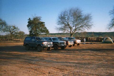 1986 Ford Bronco - Several Ford Bronco SUVs are lined up in a dusty outdoor area with a tent pitched nearby.