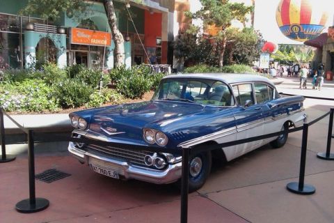 1991 Ford Crown Victoria - A classic Chevrolet sedan is displayed in front of a building with a Disney store sign.