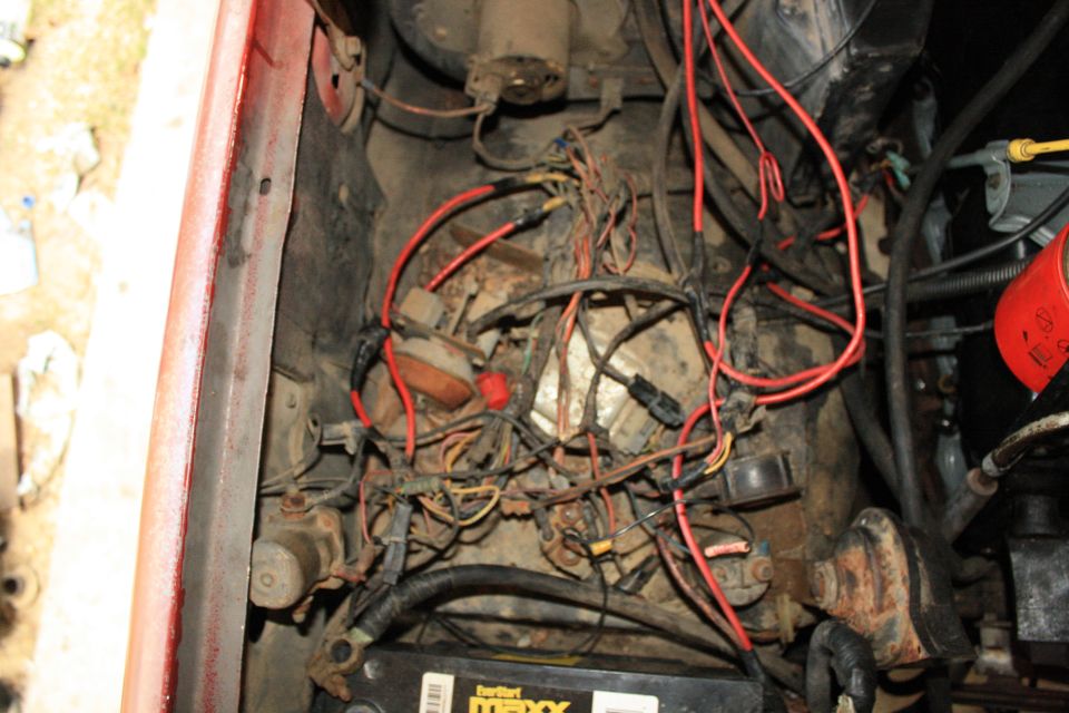 Engine bay wiring, red and black wires tangled around engine components, with a car battery visible at the bottom